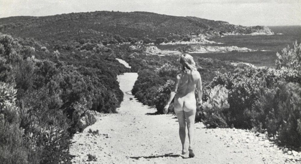 Nude woman walking along a gravel path above a seaside view