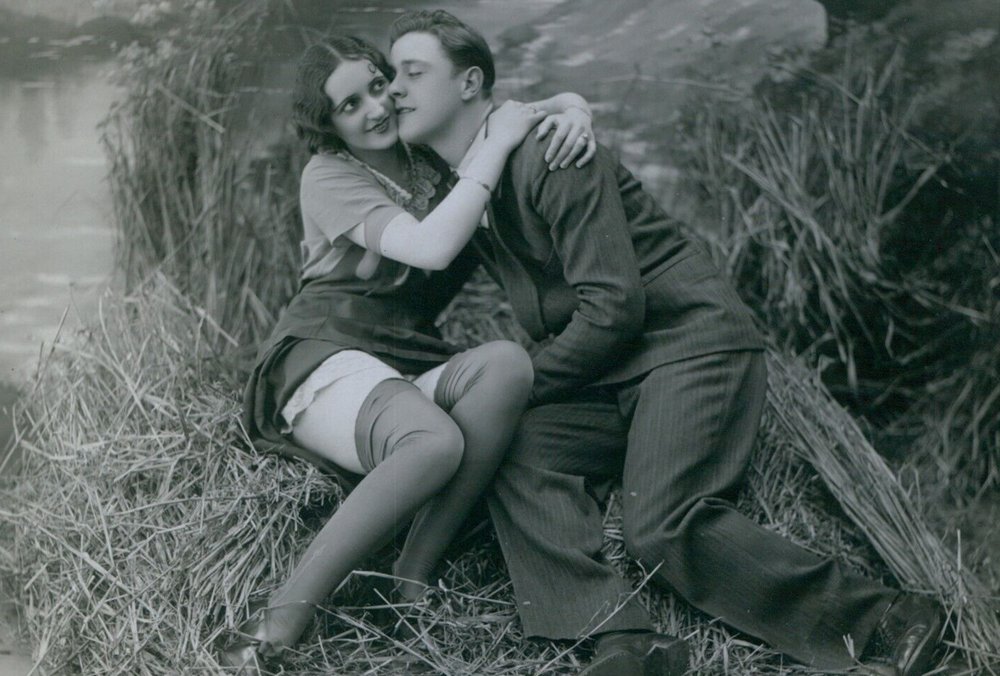 A well dressed man seduces a woman beside a small pond